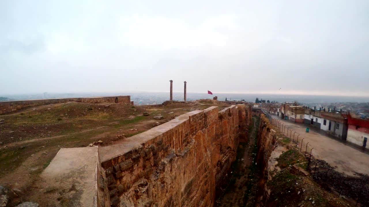 la zanja hecha a mano del castillo de urfa divide las ruinas y los barrios marginales lejos dos columnas los pájaros vuelan nieve y lluvia