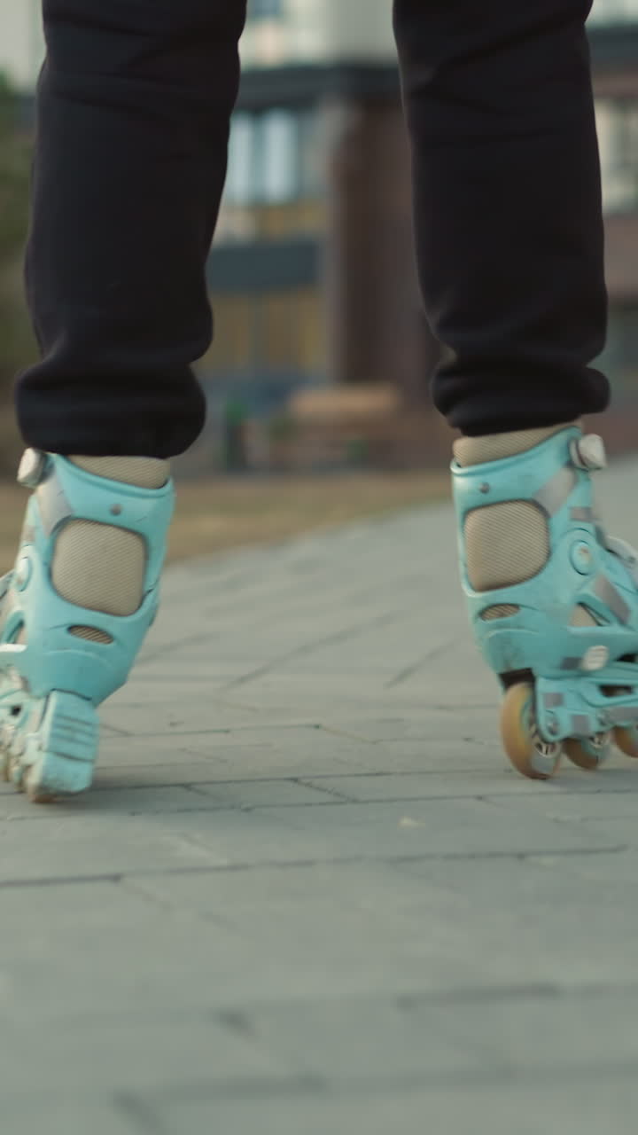 A close-up back shot of rollerblades gliding smoothly through a paved park path, with residential buildings visible in the background. focusing on the motion and the urban environment