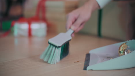 hand collecting broken bauble pieces in dustpan at home during christmas