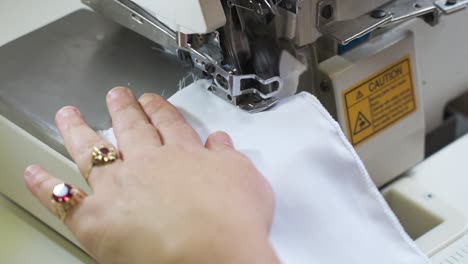 primer plano de una mano guiando una tela blanca a través de una máquina de coser industrial con precisión