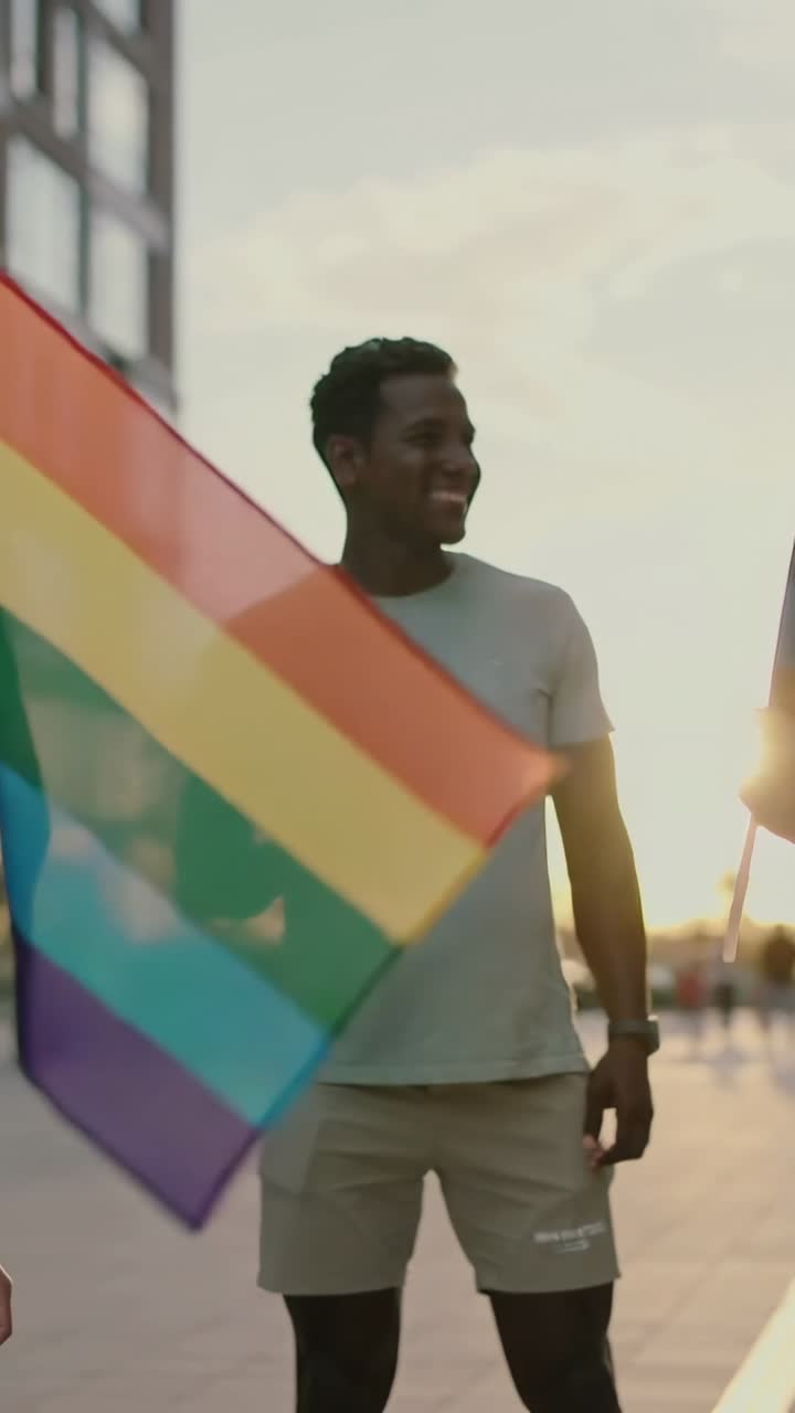 Video verticale: Uomo con bandiera arcobaleno in piazza, la brezza fa ondeggiare la bandiera rivelando il busto per il pride.