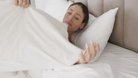 sad biracial woman lying in bed holding pillow at home, slow motion