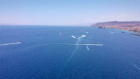 aerial view of watersports and boats on blue sea with distant mountains and port