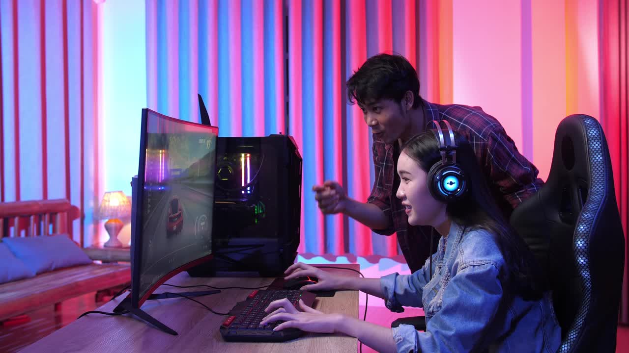 Asian Man Actively Points To A Video Playing On The Computer Screen And Explains Something To His Friend, They Win