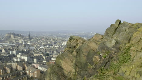 pan right to left from male and female hikers on the top of salisbury crags over to edinburgh city centre below with edinburgh castle in the background on a sunny day, scotland