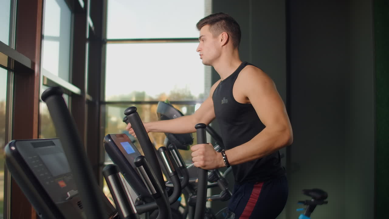 Spor salonunun kardiyo alanında eliptik bisiklette antrenman yapan bir adamın arkadan görünümü