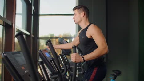 Back-view-a-man-in-the-cardio-area-of-the-gym-trains-on-an-elliptical-trainer.