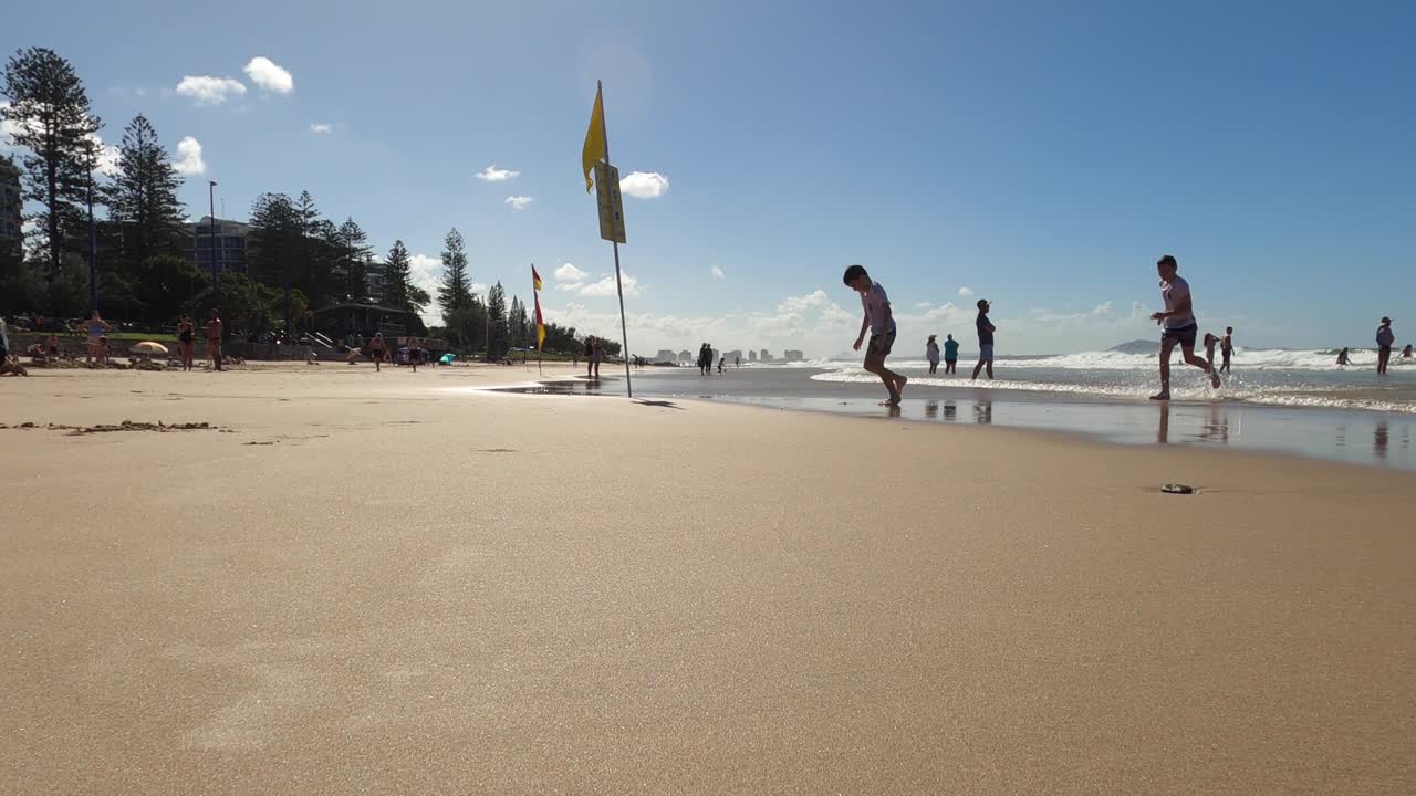 Two boys run out of the water onto a pristine beach in Australia. Low angle view.