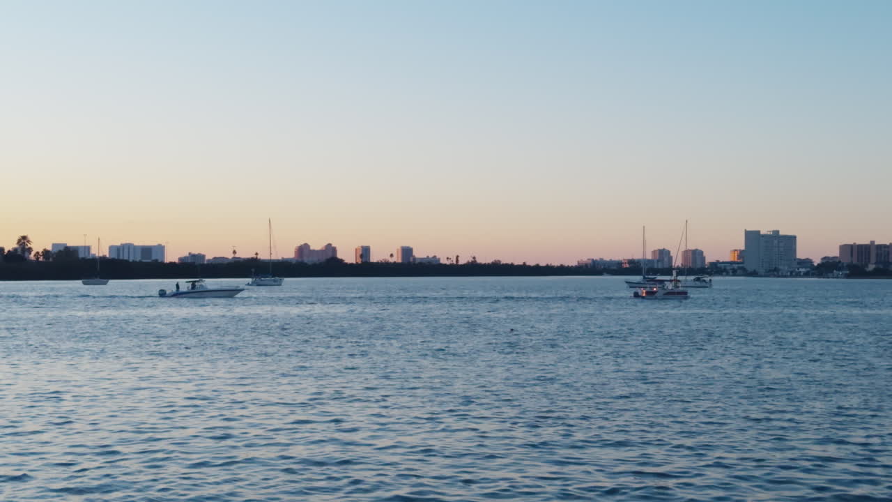 Sunlit horizon with distant shoreline silhouette buildings and boats slowly driving across Saint Joseph Sound, static establishing Clearwater Florida