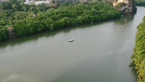 Un-Solo-Y-Solitario-Bote-De-Cola-Larga-Tailandés-Flotando-En-Un-Río-Rodeado-De-Bosques-De-Manglares-Verdes-En-La-Ciudad-De-Krabi,-Tailandia,-Durante-Una-Tarde-De-Puesta-De-Sol