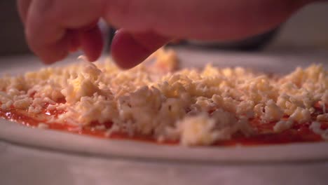 manos espolvoreando queso rallado sobre masa de pizza con salsa de tomate