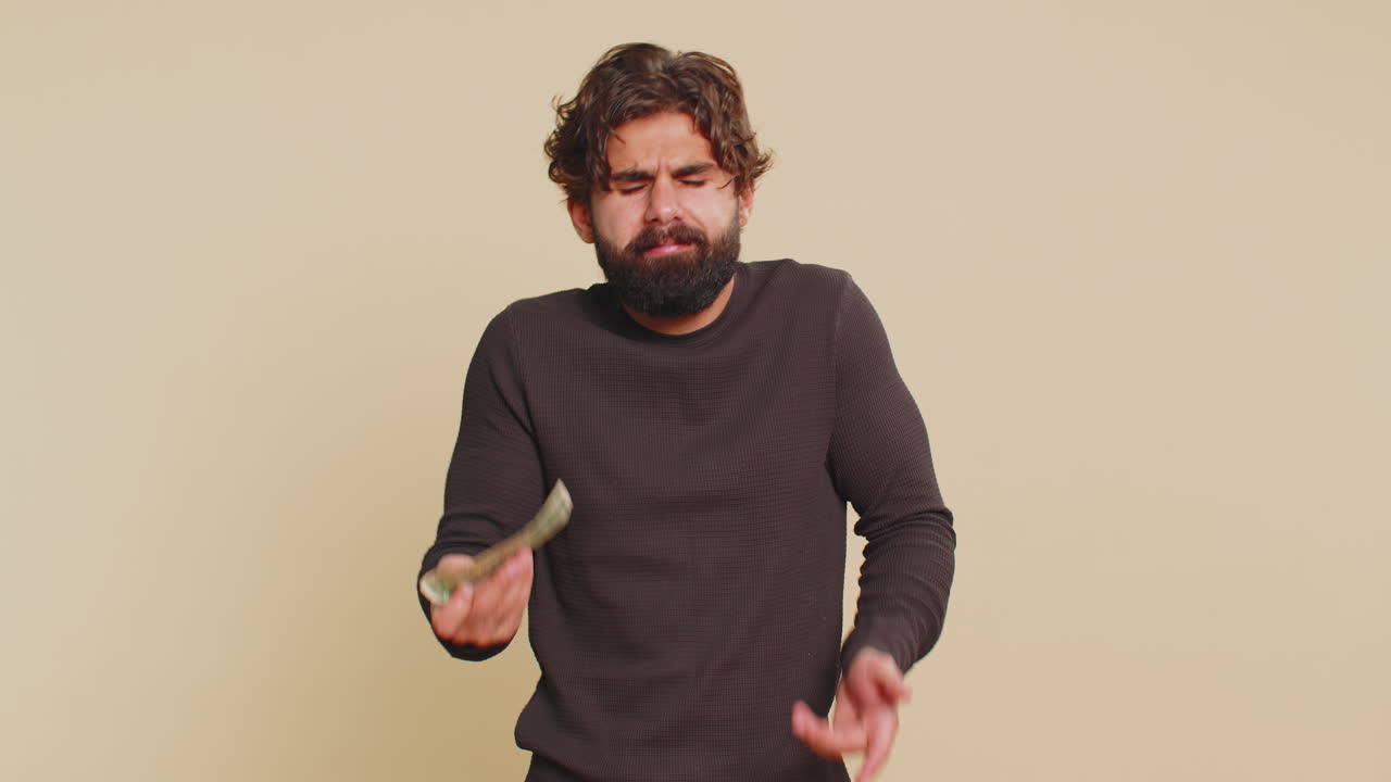 Poor man with insufficient amount of money holding one dollar banknote against beige background