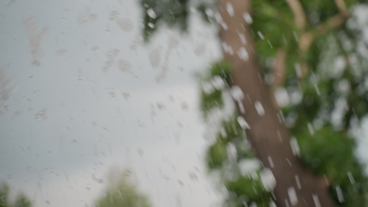 Close view of water splash rising from fountain, droplets scattering with blurred tree background, summer light catching motion, dynamic texture and soft green shapes behind