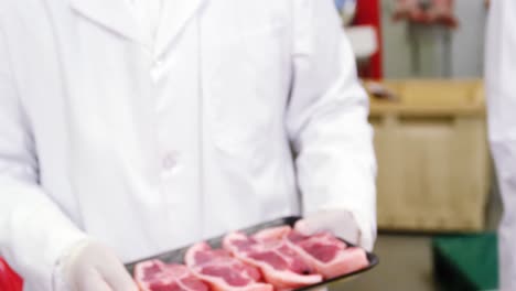 butcher holding a tray of raw meat