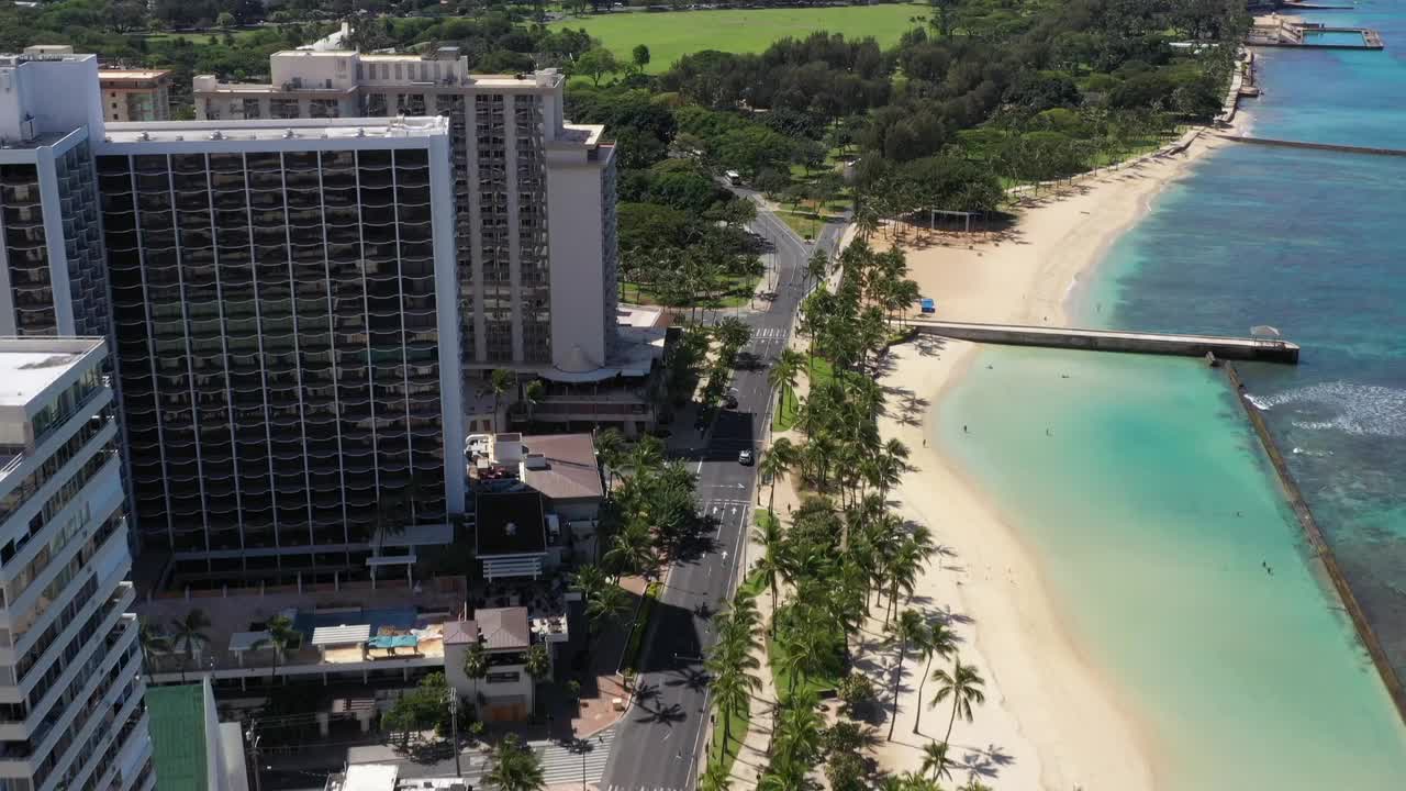 Aerial view of Hawaii city buildings, beach, and mountains under the sky. A road runs through the scene, connecting the city to the natural landscape.