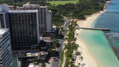 aerial view of hawaii city buildings, beach, and mountains under the sky. a road runs through the scene, connecting the city to the natural landscape.