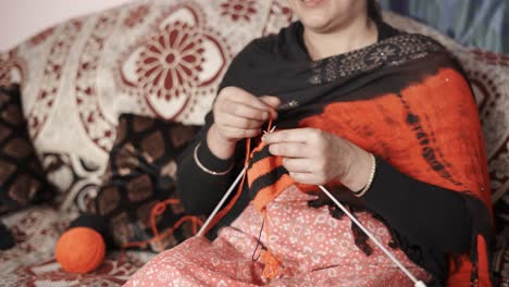 traditional indian woman siting on bed and knitting with wool in black and red color