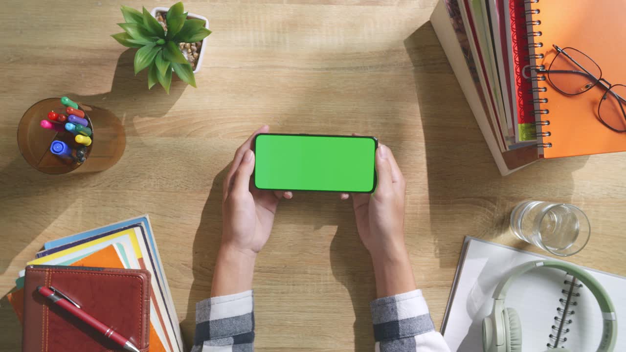 vista de arriba hacia abajo de una computadora portátil con pantalla verde simulada pantalla chromakey en un escritorio de oficina de madera al lado de la libreta con bolígrafos, gafas y un vaso de agua.