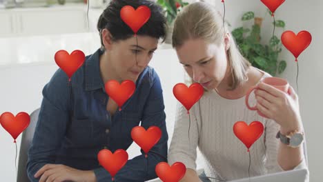 animation of heart balloon emojis over happy caucasian female couple in love drinking coffee