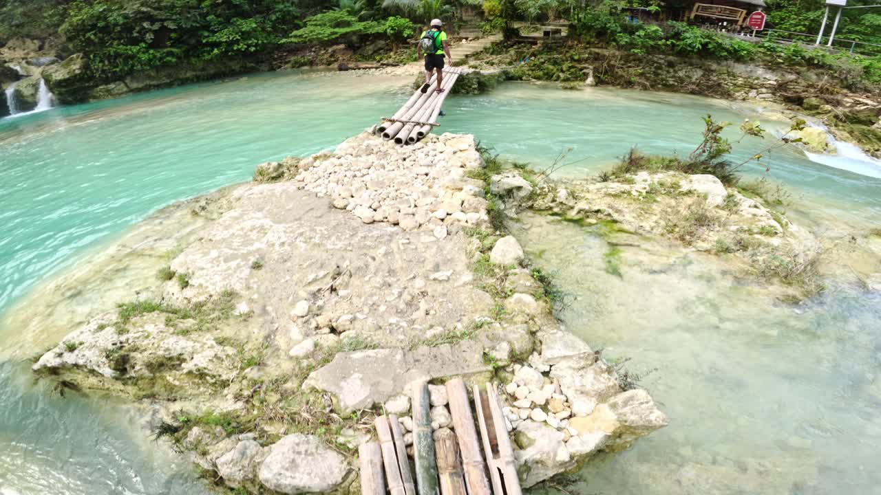 Pelancong melintasi jembatan pedesaan di atas air jernih selama pendakian hutan, Filipina