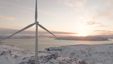 wind turbine slowly turns on white arctic mountain, vivid sunset over fjord