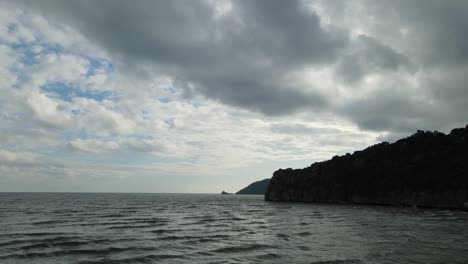 Aerial-footage-sliding-towards-the-right-over-the-sea-revealing-islands-in-the-horizon-and-a-mountain-making-a-silhouette,-gray-clouds