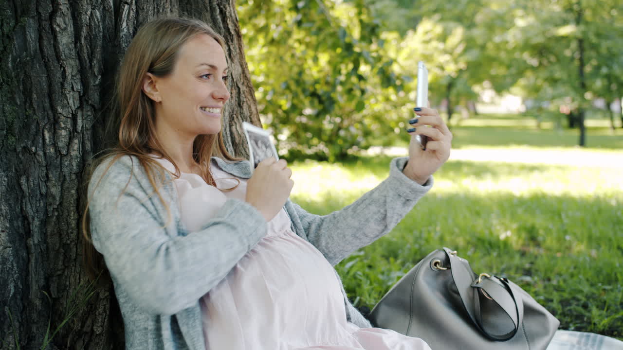 Gravid kvinde tager selfie i en park