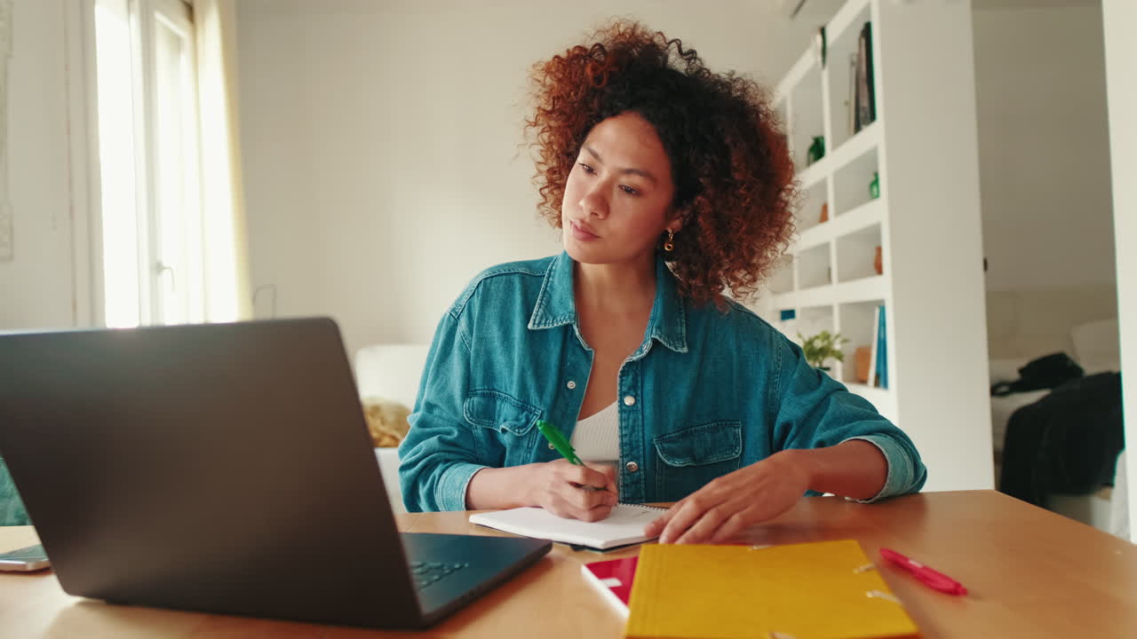 Young Woman Writing Notes While Studying with Laptop at Home