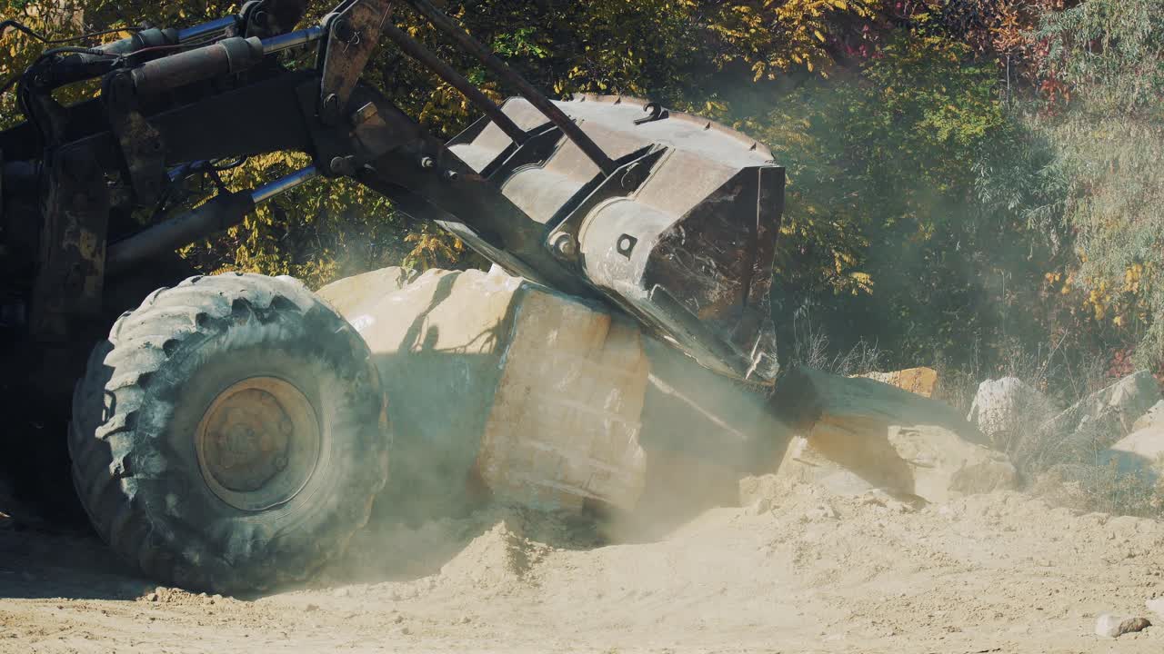 Old rusty excavator in a granite quarry pours sand from a bucket. Dust and stones under the wheels. Loading work