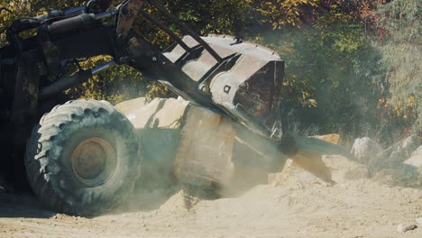 old rusty excavator in a granite quarry pours sand from a bucket. dust and stones under the wheels. loading work