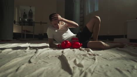 serene male boxer reclines on floor of gym taking rest after intensive efforts to enhance strength and body shape. relaxing after engaging in sport of boxing at sports club