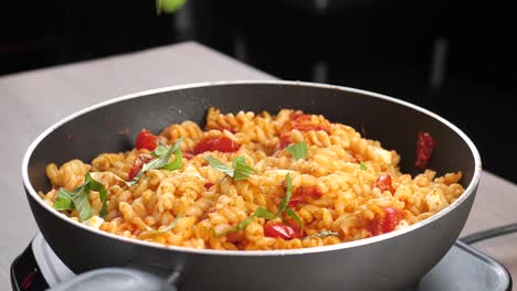 scatter freshly cut basil leaves on hot and creamy fusilli pasta with tomato sauce in large pan