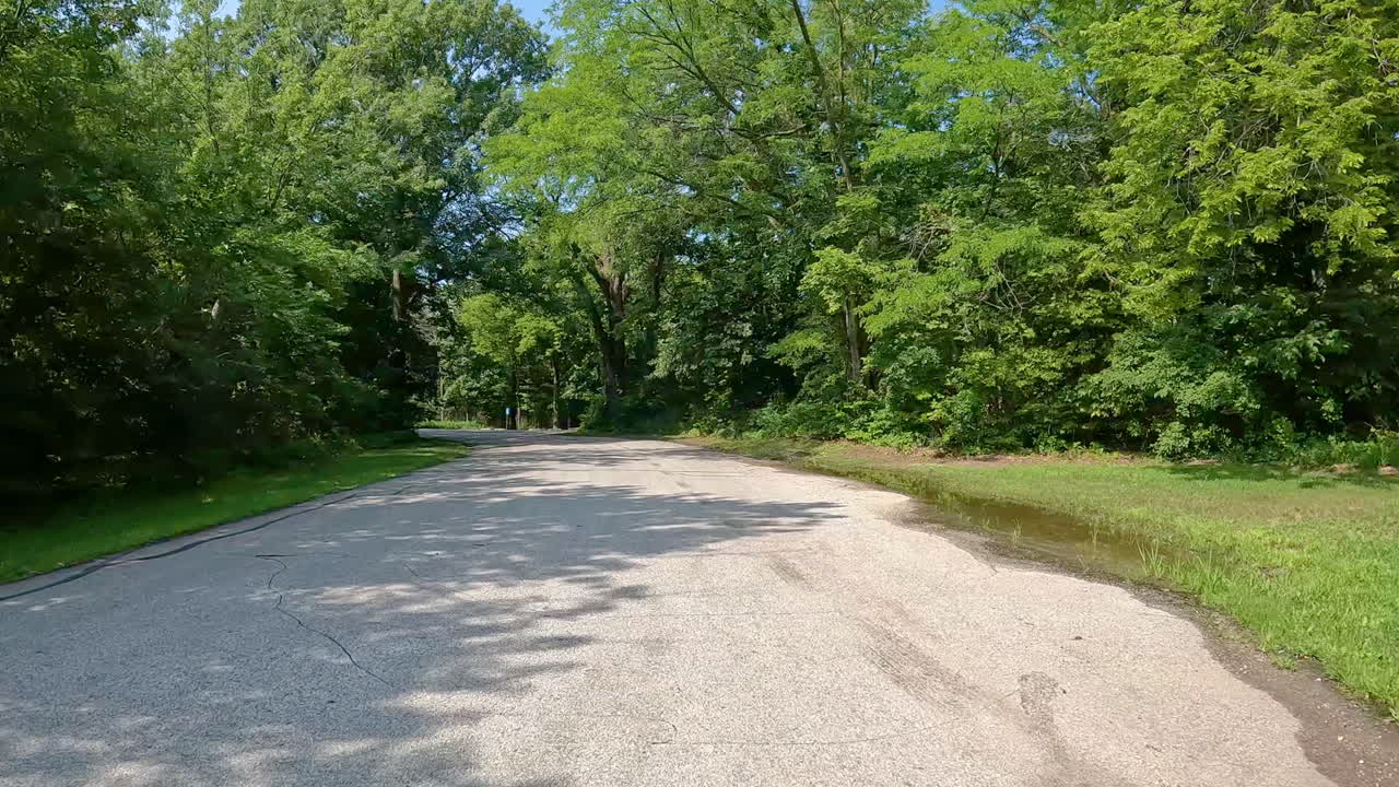 POV - driving on paved road thru Jester County Park in the Des Moines River Valley in central Iowa; driving past the one of the trailhead parking areas with a stone outhouse; vacation, holiday