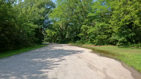 pov - driving on paved road thru jester county park in the des moines river valley in central iowa; driving past the one of the trailhead parking areas with a stone outhouse; vacation, holiday