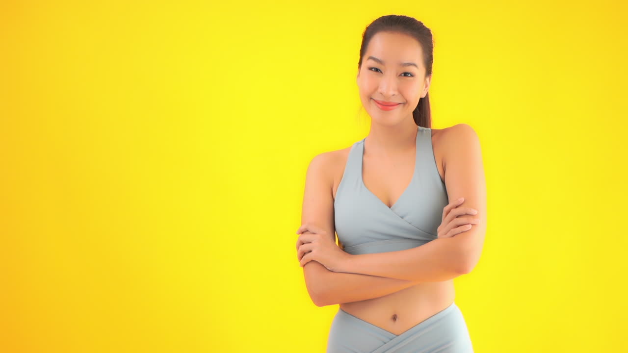 Satisfied asian female in sport clothing crossing her hands. Healthy lifestyle concept, slow motion, isolated on yellow background