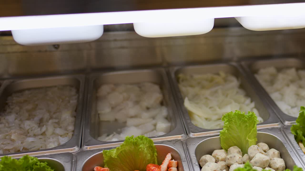 Assorted raw noodles and vegetables arranged in trays under bright lighting at an Asian buffet