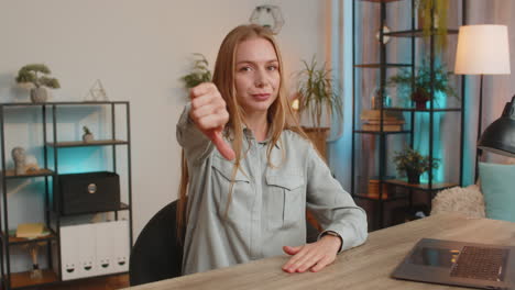 upset unhappy woman girl showing thumb down sign gesture expressing discontent sitting at table