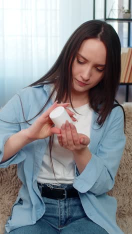 young woman suffering toothache holding cheek in pain tiredly searching and taking painkiller pills