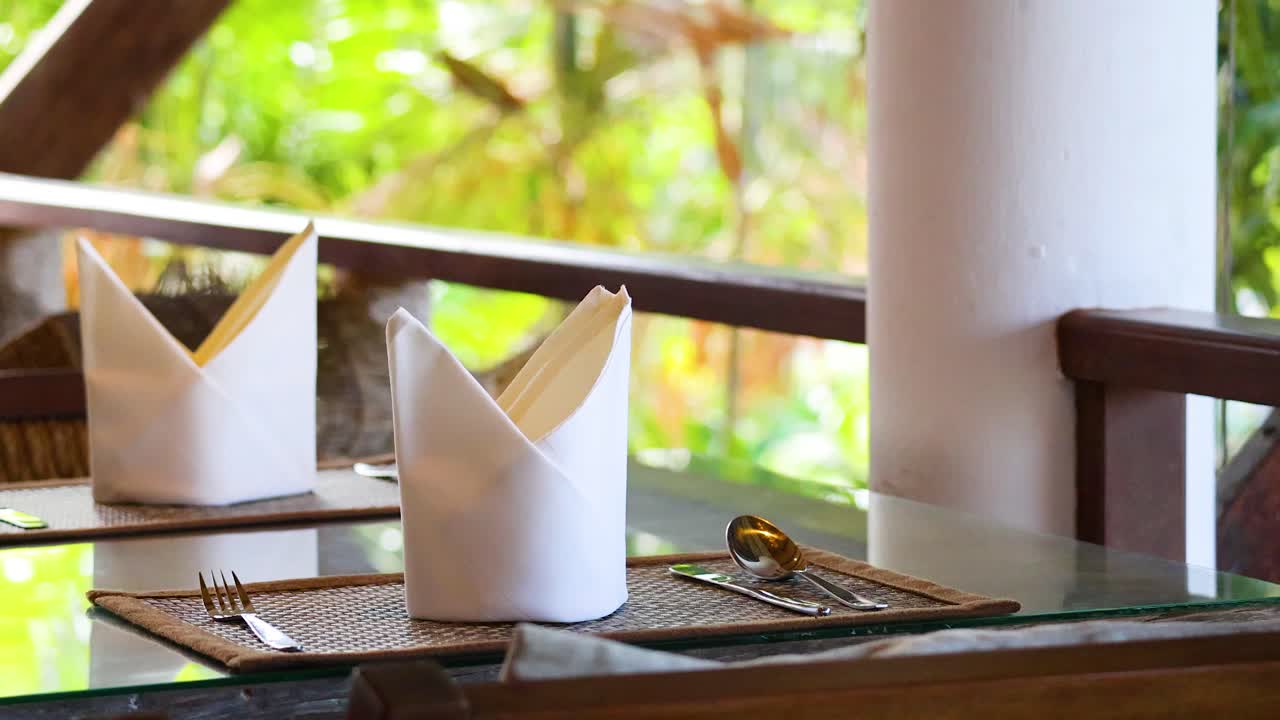 Elegant table setting with folded napkins and cutlery on a balcony overlooking lush greenery in natural light
