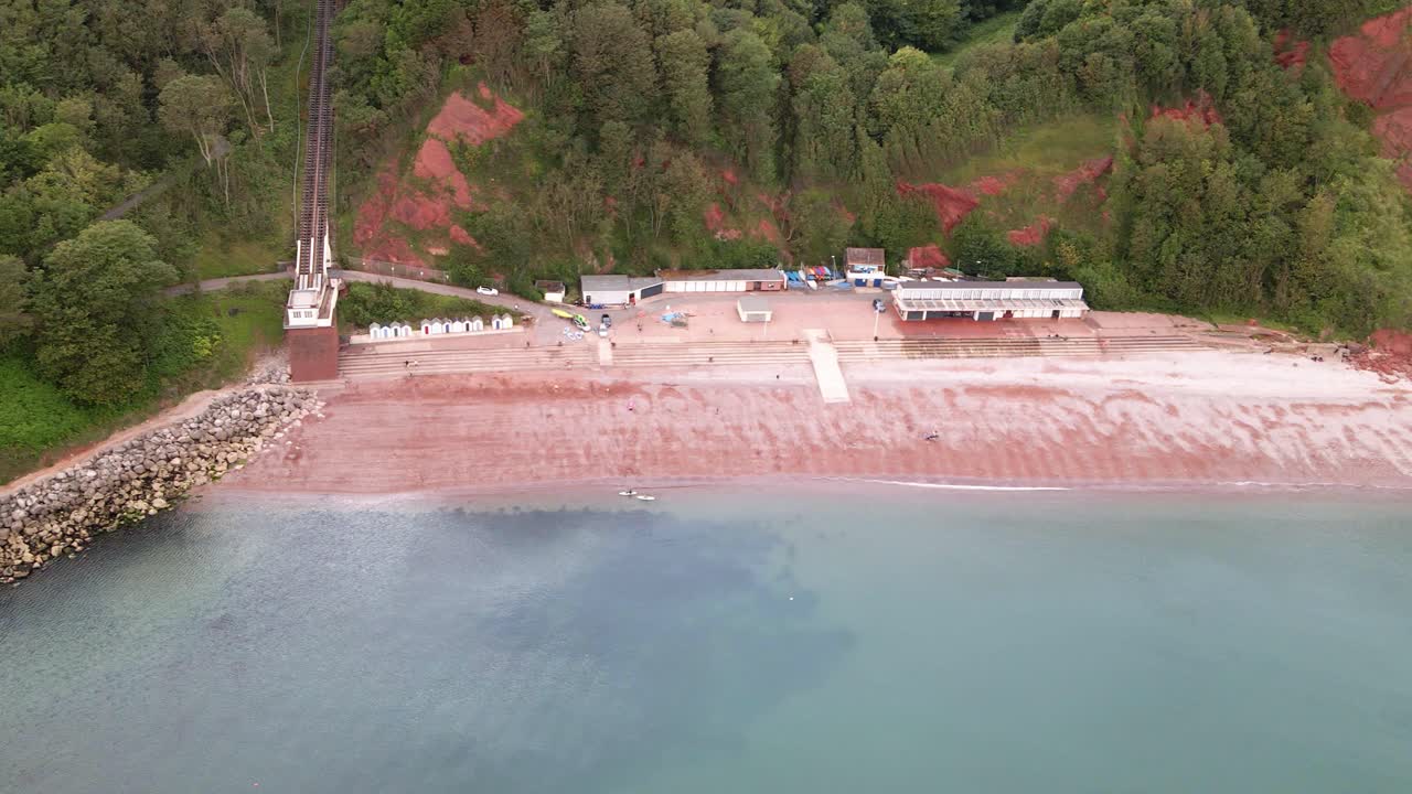 vuelo aéreo en carro que muestra la popular playa de oddicombe con agua azul del océano, arena roja y acantilados de brechas