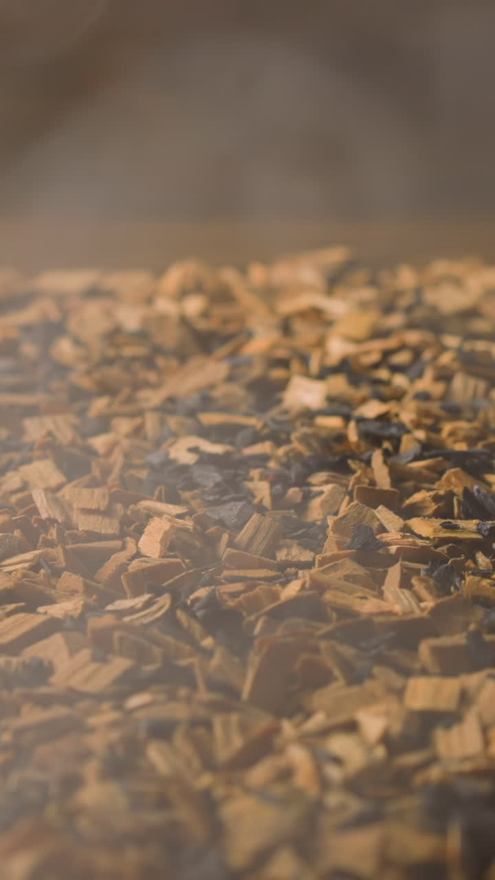 Heap of small wooden chips and hot charcoals with light steam flow rising up to cook smoked food products in smokery closeup slow motion