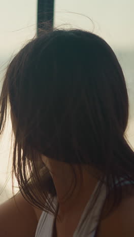 young woman sits on boat looking at foamy water surface dreamily side view. silhouette of female on background of blurred sea water closeup. wind blows lady hair slow motion