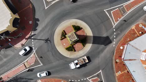 overhead drone footage captures cars and trucks moving through a sunlit roundabout in a small australian town, with steady camera and clear shadows