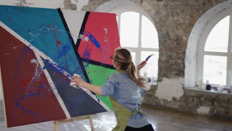 woman uses wide brush and color paints splashing gesture on canvas in artstudio