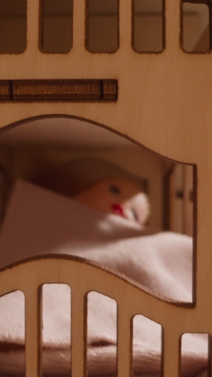 Una bambola carina giace sotto un piumino in tessuto pile su un letto giocattolo di legno a due livelli in una casa delle bambole, mentre il sole sorge e un nuovo giorno inizia, primo piano con zoom indietro.