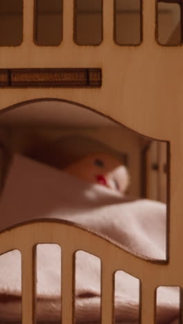 cute doll lies under fleece fabric comforter on toy two-level wooden bed in dollhouse while sun rises up and new day begins closeup zoom out