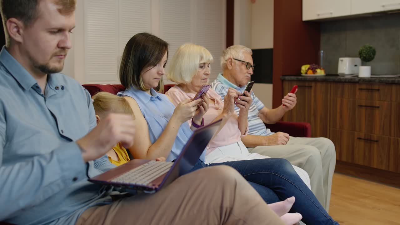 A family using their phones and a laptop together on a couch