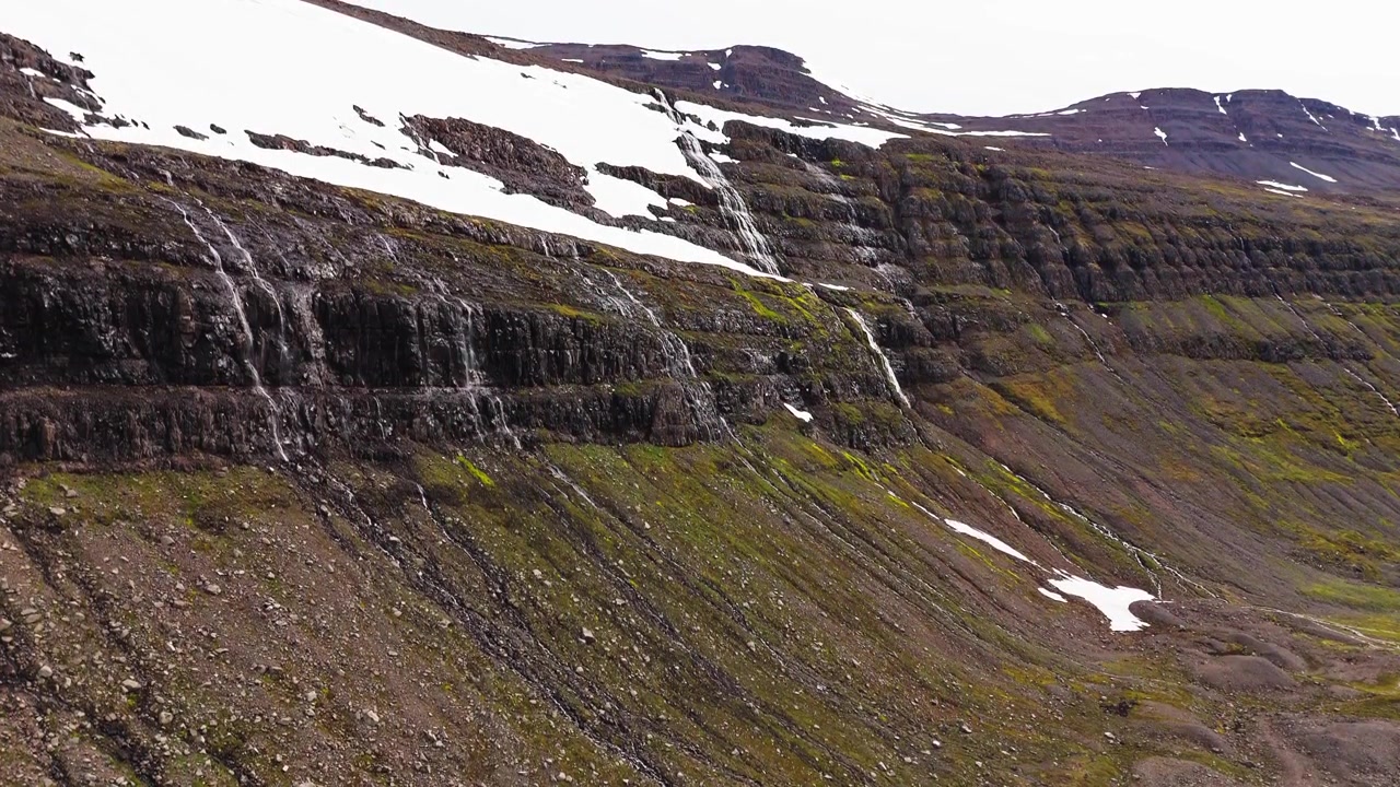 Spettacolare ripresa aerea cinematografica di neve che si scioglie e molteplici cascate che scendono da scogliere rocciose a Drangajokull, Islanda, evidenziando la sostenibilità e il cambiamento climatico.