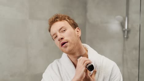 cute young man shaves his beard with an electric razor