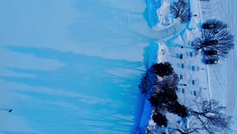 4k winter aerial flyover sunset reflection shadow trees snow covered park skate path next to benches and parking lot connected to canada's largest manmade ice rink adults skating edm victoria park4-6